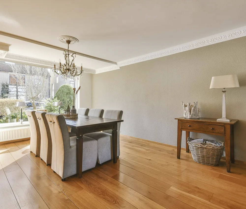 Warm golden oak wide plank wood flooring in a sunlit dining room with a dark wood table.